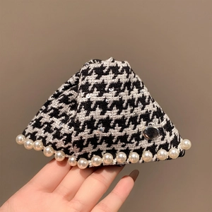 Detail of houndstooth shark hair clip with white pearls and metal logo plate