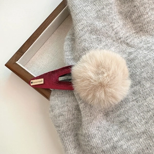 Gros plan d'une barrette en velours côtelé bordeaux avec pompon et étiquette dorée