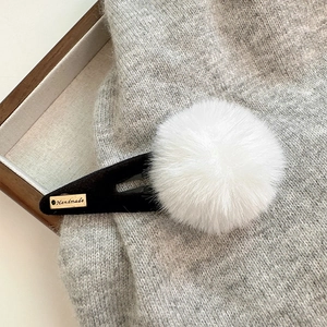 Détail d'une pince à cheveux à pompon blanc en fausse fourrure avec étiquette dorée
