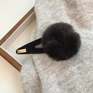 Détail d'une pince à cheveux à pompon noir avec étiquette dorée faite à la main