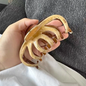 Detail view of large amber and cream marble hair claw clip held in hand for scale