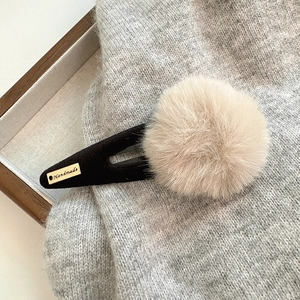 Détail d'une pince à cheveux en peluche beige avec plaque dorée Handmade sur tricot gris