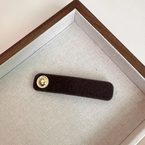 Minimalist brown flocked hair clip with gold metal button detail in aesthetic display