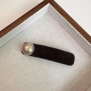 Close-up of a velvet-wrapped hair clip featuring a large champagne pearl on a wooden tray