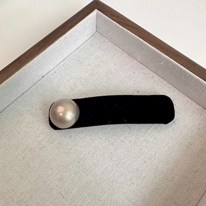 Elegant black velvet hair clip featuring a large iridescent pearl on textured background