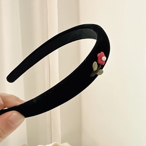 Close-up of black velvet headband featuring a small red flower and white faux pearl detail