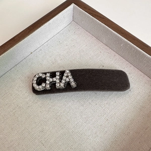 Close-up of grey flocked hair clip with sparkling rhinestone CHA lettering detail