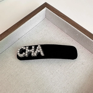 Detail of a black velvet hair clip featuring a sparkling rhinestone CHA letter design