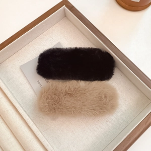 Plush faux fur hair clips in black and beige displayed on a wooden jewelry tray