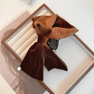 Détail d'une pince à cheveux en velours marron avec nœud et accent doré sur plateau