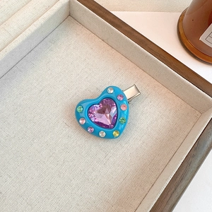 Close-up of heart-shaped hair clip with colorful crystals and a purple gemstone center