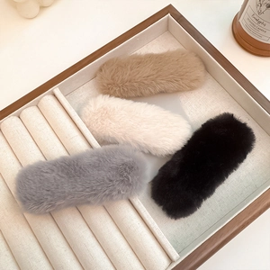 Detail of four colorful plush hair clips displayed in a premium wooden jewelry tray