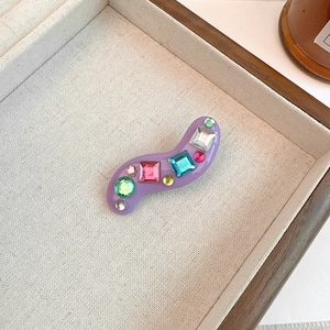 Detail of wave-shaped purple resin hair clip with colorful mixed rhinestones in Y2K style