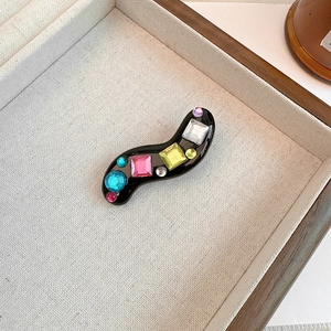 Macro shot of wavy black hair clip with colorful square and round rhinestones