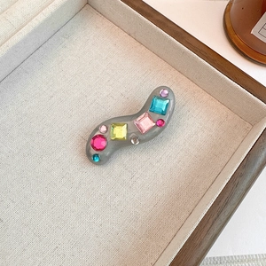 Detail of wavy resin hair clip featuring colorful rhinestones on a beige textured tray