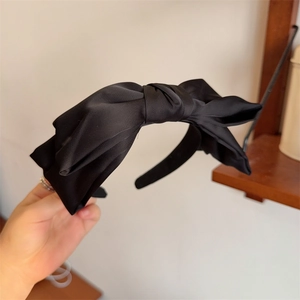 Detail of a large black satin bow headband with elegant silky texture and vintage style