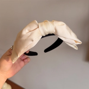 Close-up of cream satin bow headband featuring elegant silk texture and fabric folds
