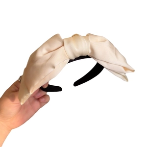 Elegant cream satin large bow headband for women with a black base shown on white background