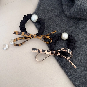 Set of leopard print bow hair ties with pearls and silver hoop earrings on neutral fabric