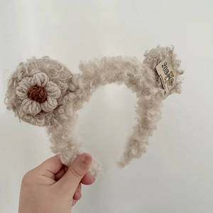 Detail of plush beige headband featuring a crocheted flower and vintage bear tag