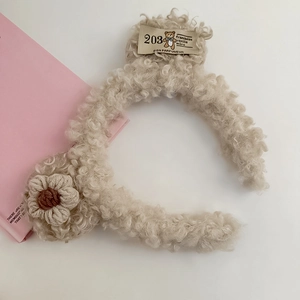 Detailed view of beige plush fleece headband with knitted flower and woven label detail