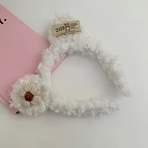 Close-up of white plush headband with a knit flower and vintage bear fabric label detail