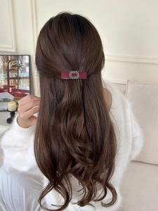 Detail of burgundy hair clip with sparkling rhinestones worn on wavy brown hair