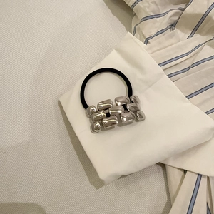 Close-up of black elastic hair tie with silver geometric metallic block accents