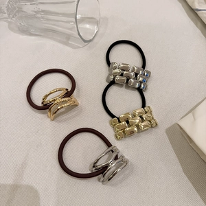 Close-up of modern hair ties set with metallic square and ring details on white texture