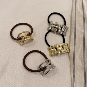 Close-up of four elastic hair ties with square and curved metal alloy accents