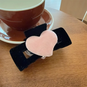 Détail d'une pince à cheveux cœur en velours rose avec base en peluche noire sur bois