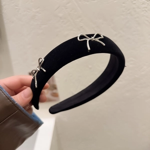 Serre-tête large en velours noir élégant avec boucles argentées tenu à la main