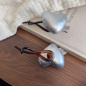 Elegant satin-finish heart hair clips in black and amber colors on a wooden surface