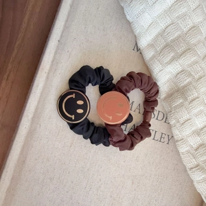 Detail of black and brown scrunchies with smiley face charms on woven fabric background