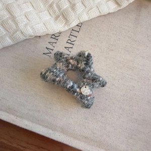 Detailed close-up of a star-shaped tweed hair claw with a metallic logo tag decoration