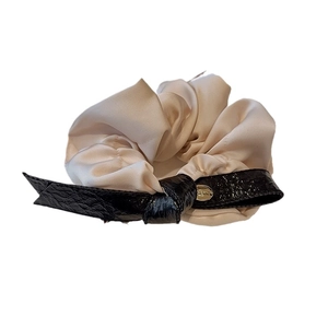 Elegant beige satin hair scrunchie with black faux leather bow and gold metal logo charm