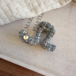 Macro shot of grey tweed fabric claw clip with 5 PARIS gold metal tag detail