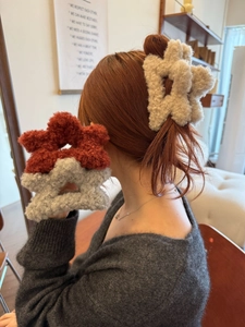 Dettaglio di grandi mollette per capelli in peluche a fiore nei colori beige e grigio
