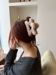 Dettaglio di un fermaglio per capelli a fiore in peluche beige indossato sulla nuca