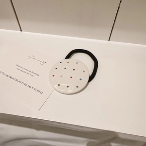 Détail d'un élastique à cheveux noir avec un accent blanc serti de strass colorés