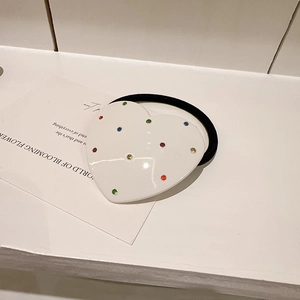 Détail d'un élastique à cheveux blanc en forme de cœur avec strass colorés et élastique noir