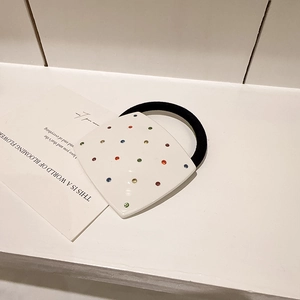 Détail d'élastique à cheveux en acétate crème avec strass colorés sur une carte blanche