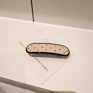 Détail d'une pince à cheveux en acétate crème avec strass colorés et bordure noire