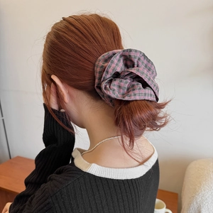 Pink and green plaid fabric scrunchie shown on a ponytail in a warm indoor setting