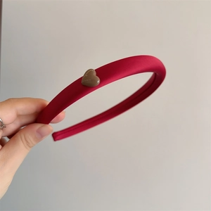 Close-up of a burgundy satin headband with a small dark brown heart-shaped ornament