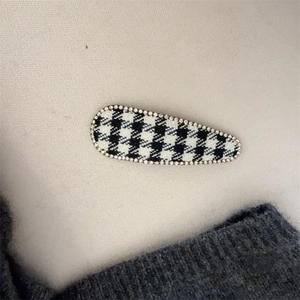 Detailed view of houndstooth hair clip with sparkling rhinestone edges on beige fabric