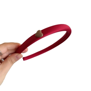 Red satin padded headband with brown 3D heart decoration held by hand on white background