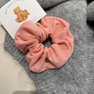 Close-up of pink scrunchie with soft towel fabric texture and golden metal tag detail