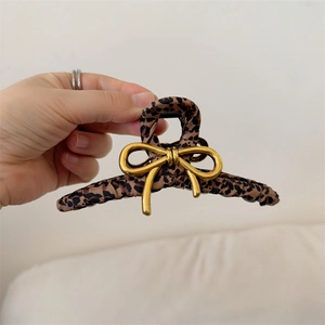 Detail of leopard print fabric hair claw clip featuring a gold metal bow accessory