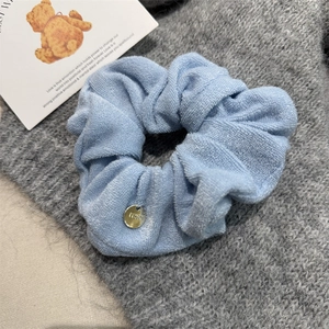 Close-up of light blue fabric scrunchie with metallic gold logo tag on knit texture